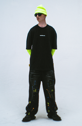 Model in the Haresquare Black T-shirt with a white print, styled with Haresquare paint splash black denim jeans and designer sunglasses – unisex luxury sportswear from Ireland.